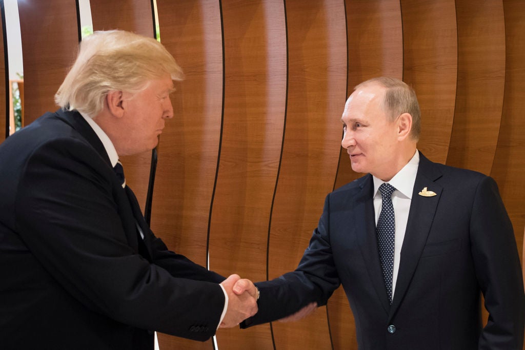 Donald Trump and Vladimir Putin shake hands in front of a wood backdrop.