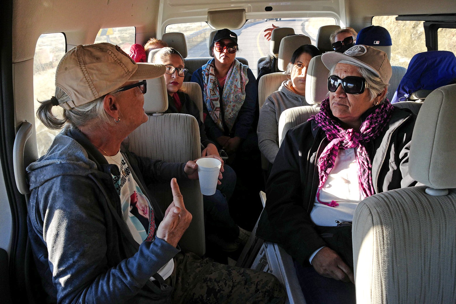 Buscadoras in a vehicle chat animatedly and hold cups of coffee en route to a search for remains of the disappeared in November 2022.