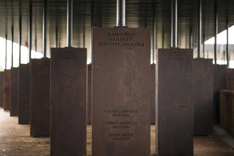 Markers held by poles connected to the ceiling of the National Memorial for Peace and Justice display locations and names on earthy brown-colored rectangular markers.