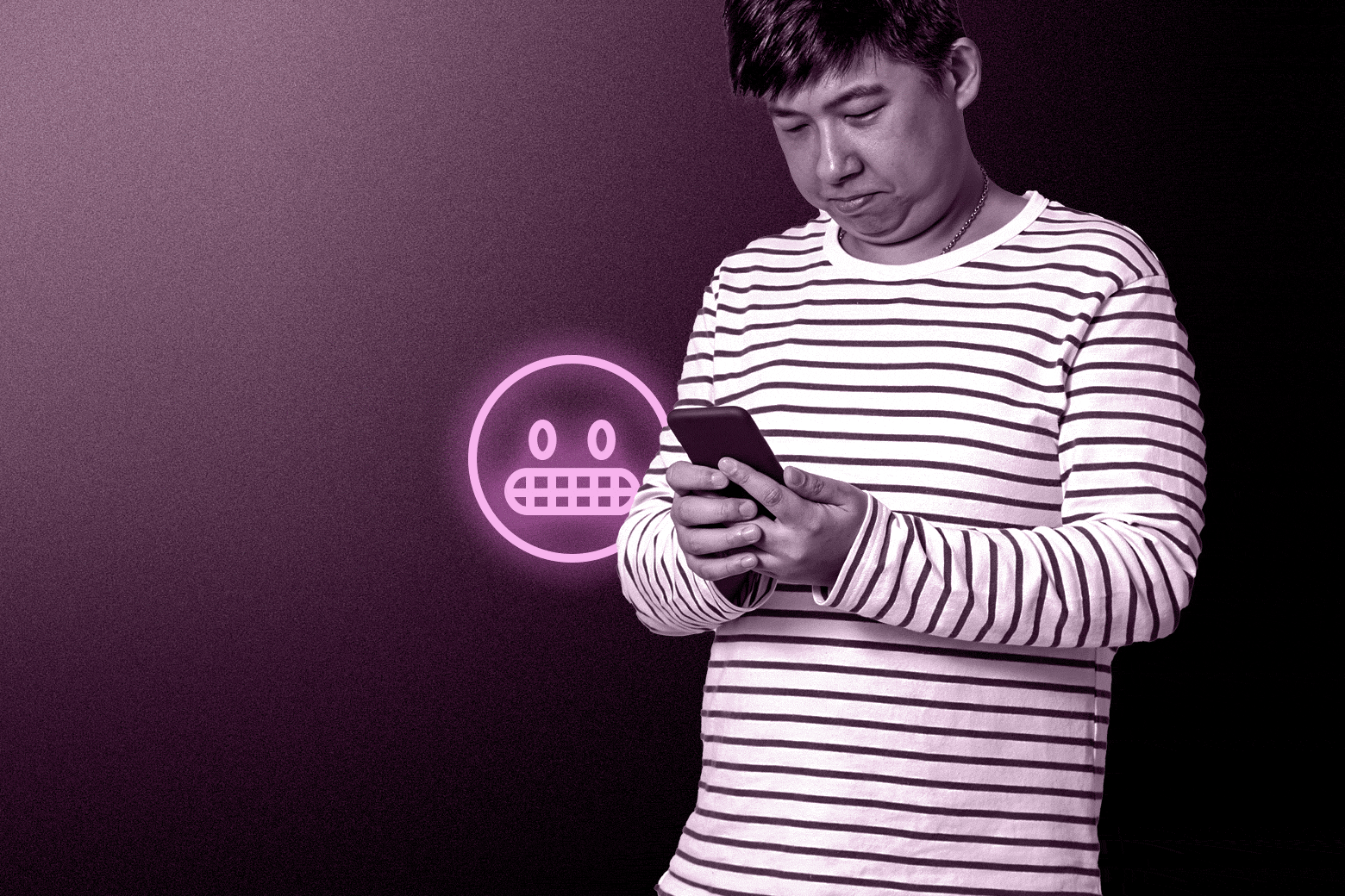 An Asian man in a black and white striped shirt looks down and texts on his phone with an awkward neon pink emoji next to him.