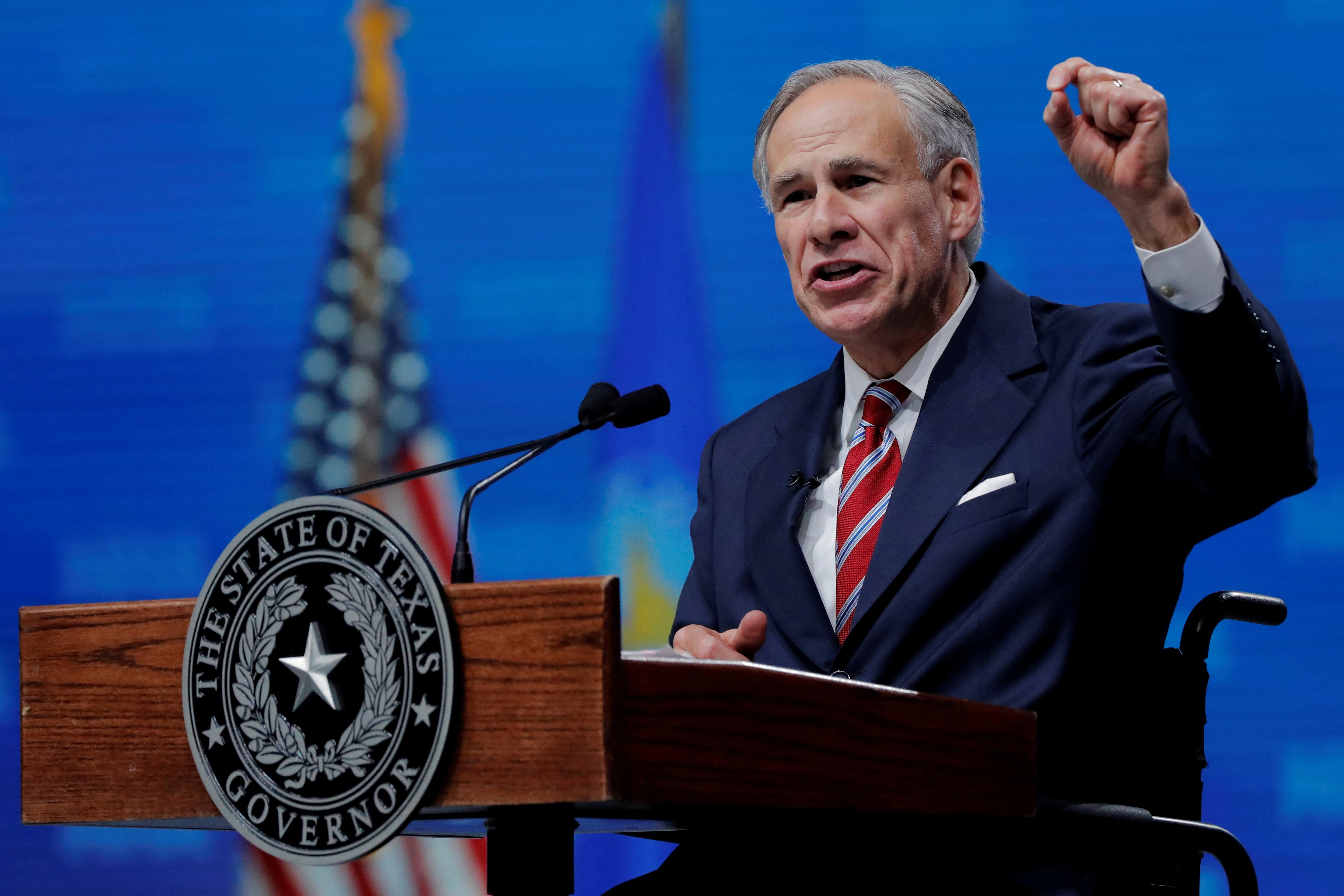 Greg Abbott gestures while speaking at a podium at a convention with an American flag in the background.