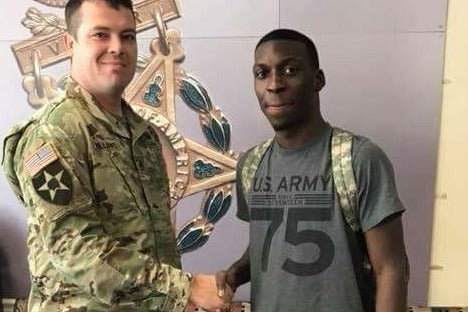 Bradford in an army tee shirt smiles and shakes hands with a man in an army uniform.