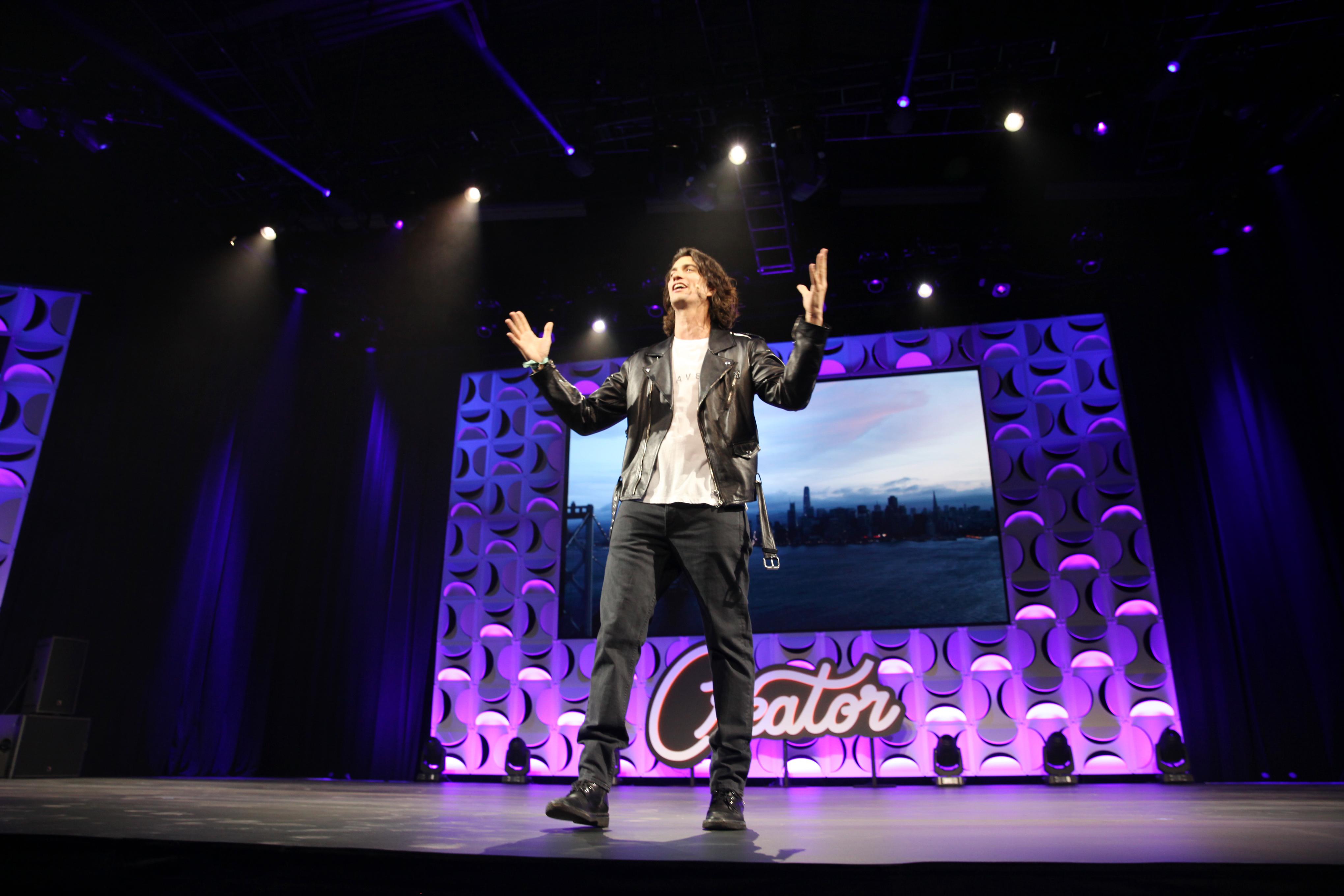 Adam Neumann is on stage wearing a leather jacket and sneakers