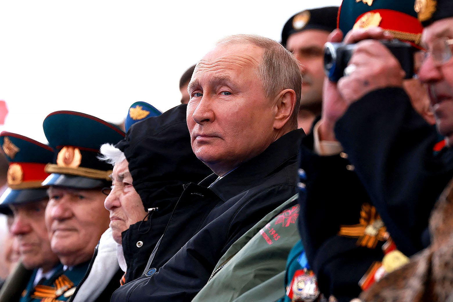 Putin in a dark overcoat surrounded by men in ceremonial military dress outside.
