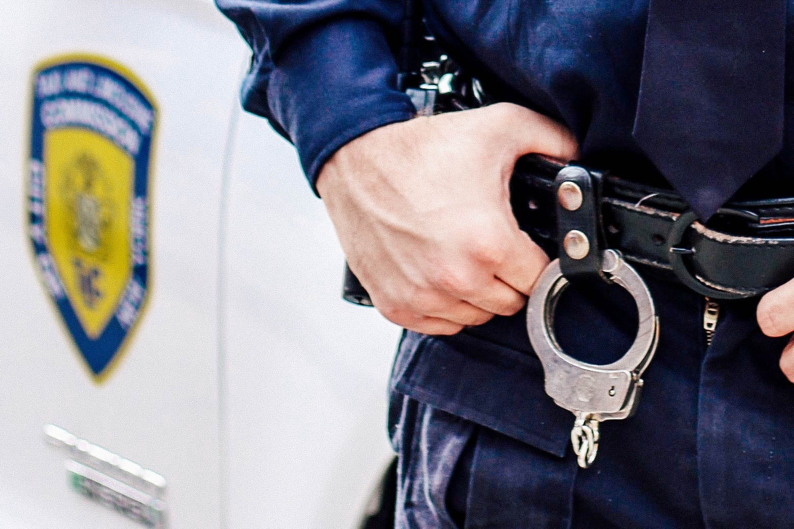 A police officer gripping his duty belt, which has handcuffs hanging off of it