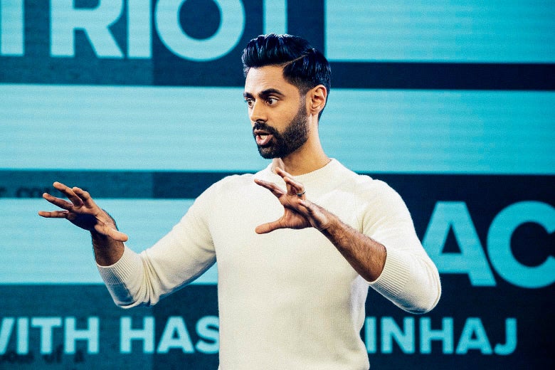 Hasan Minhaj standing with his arms raised on the stage of his show, Patriot Act.