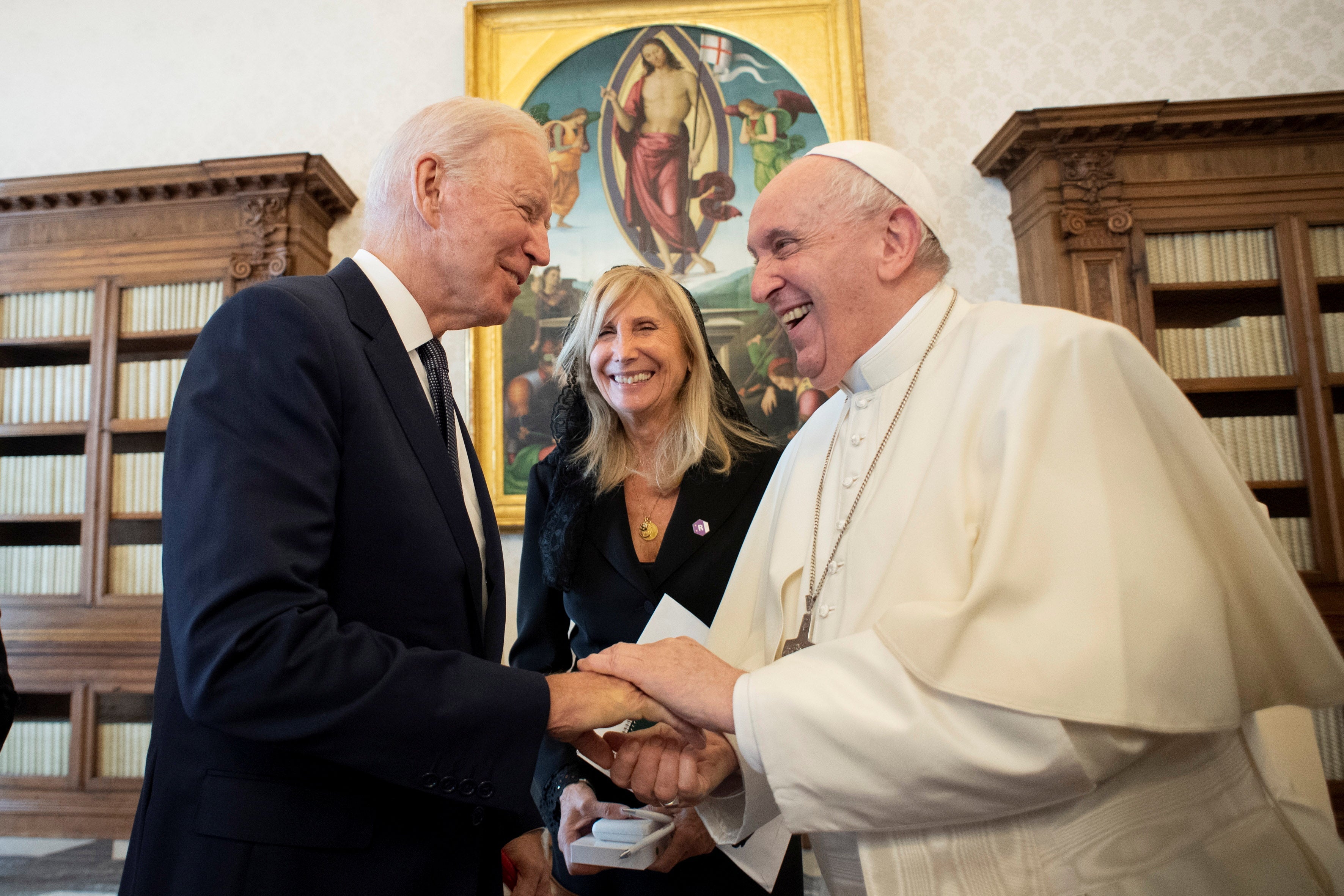 Pope Francis and Joe Biden hold each other's hands while talking and smiling.