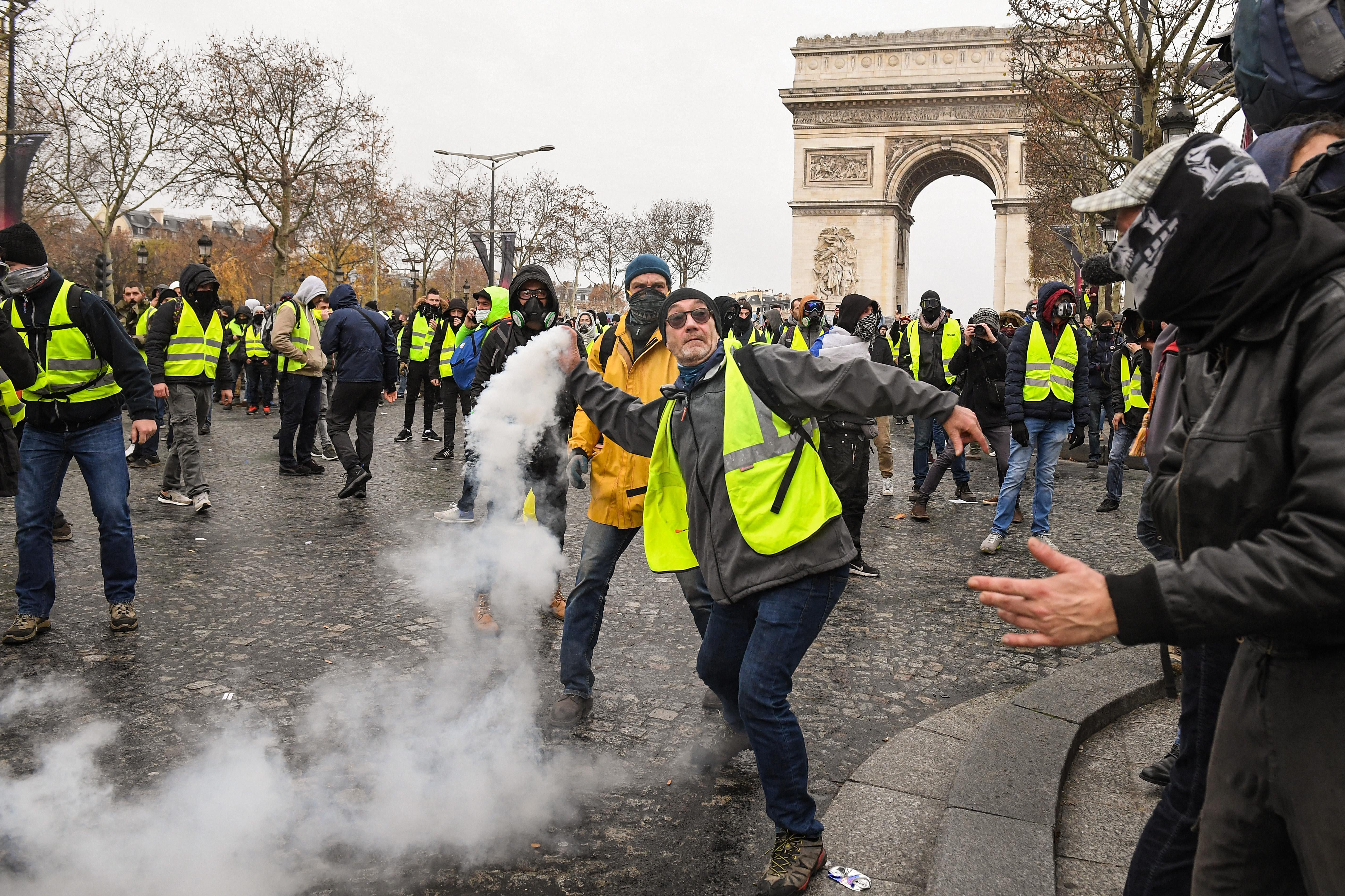 A demonstrator throws a tear gas canister during the demonstration of the yellow vests near the Arc de Triomphe on December 8, 2018 in Paris France. 