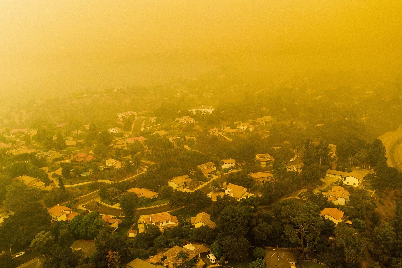 An aerial view of houses in a neighborhood beneath a cloud of orange smoke.