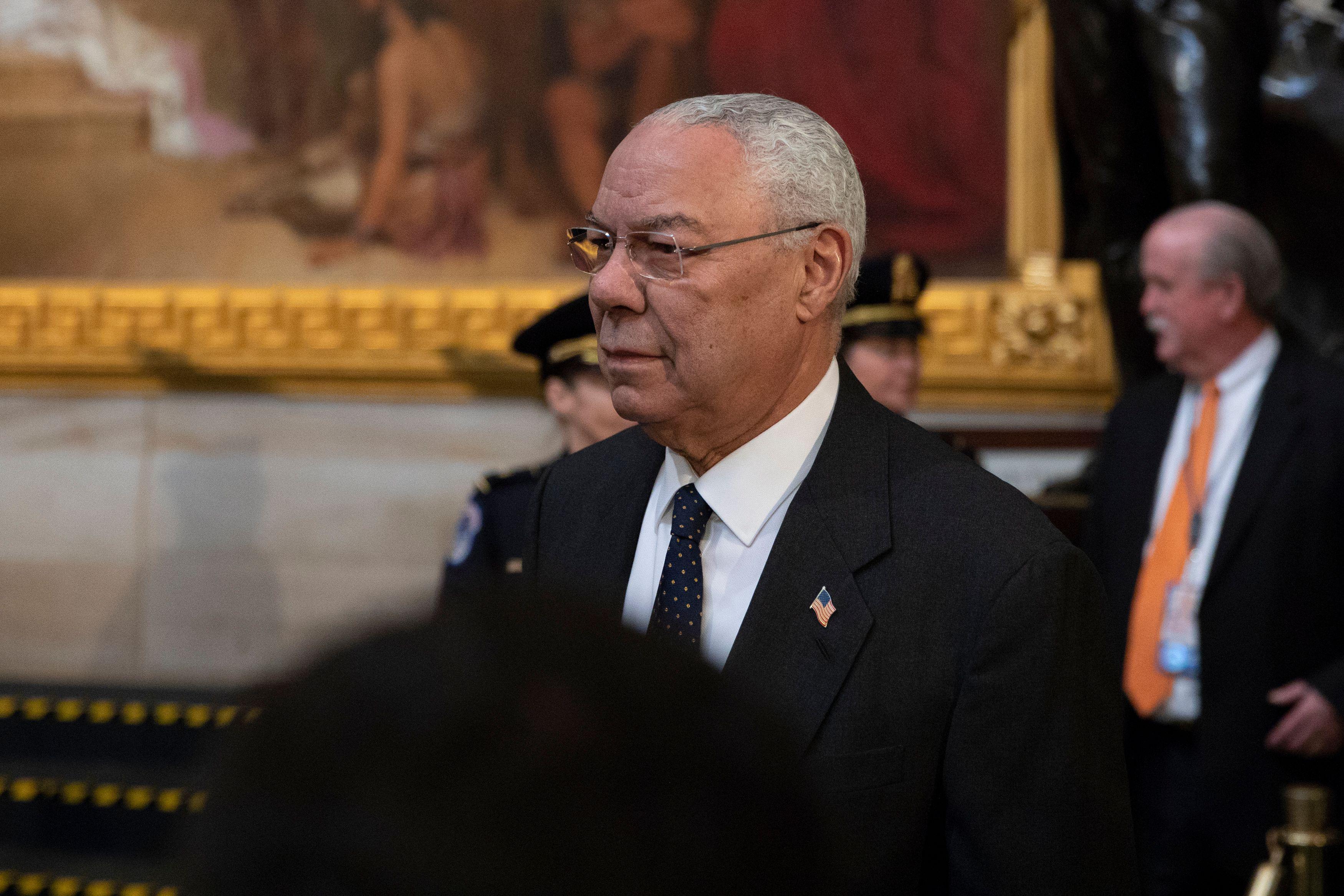 Colin Powell, with a painting and a security guard in the background