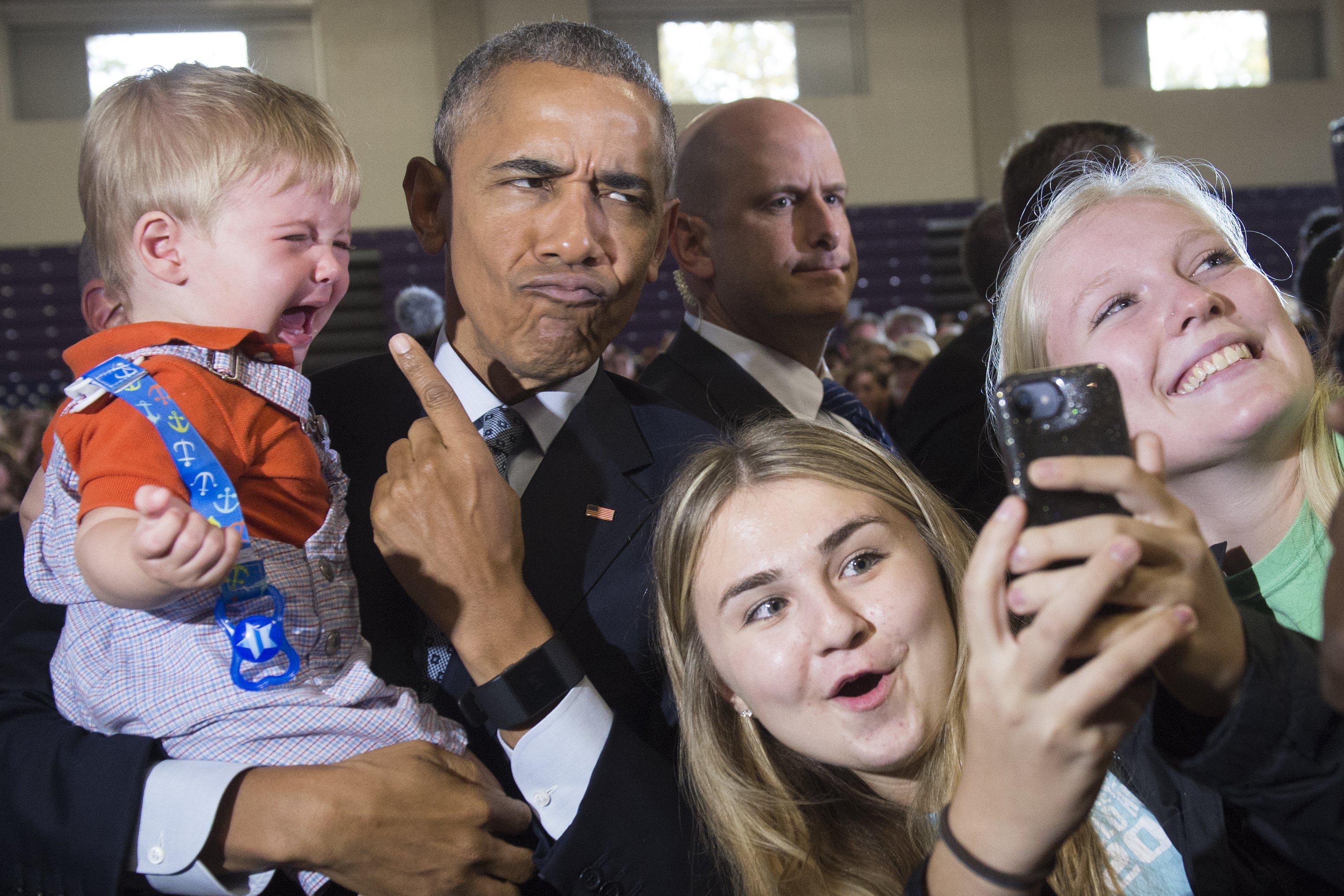 President Obama makes a silly face while he points to and holds a crying baby and two girls lean in for pictures.