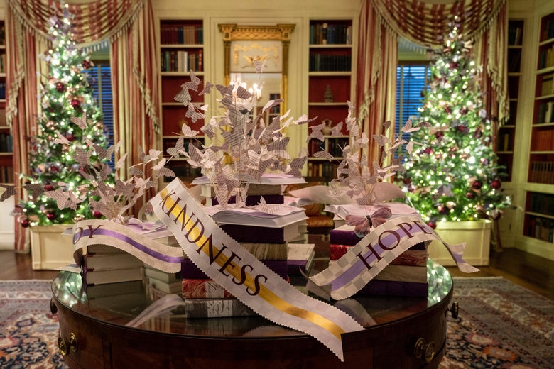 The library contains a table with a display of books and banners and paper butterflies, and in the background are two Christmas trees decorated with lights.