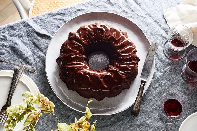 A beautiful chocolate bundt cake, covered in chocolate ganache, sits in the center of a table with glasses of Passover wine.