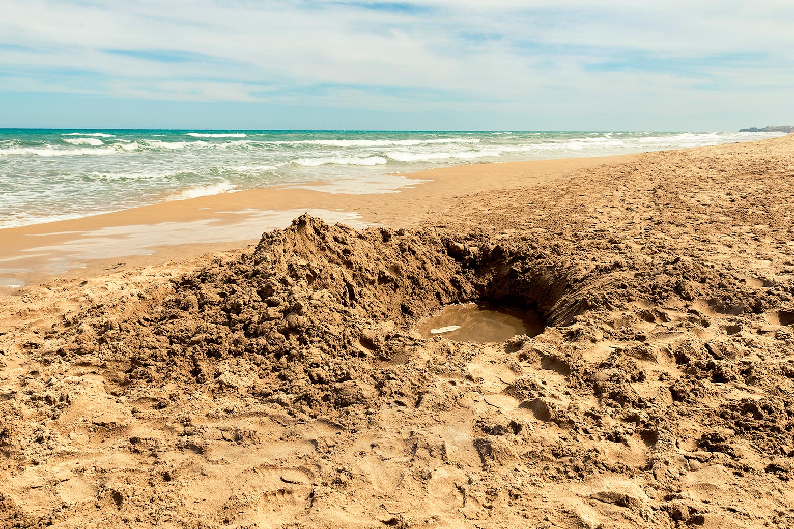 A hole that has been dug on the beach has filled with water and no one is around. 