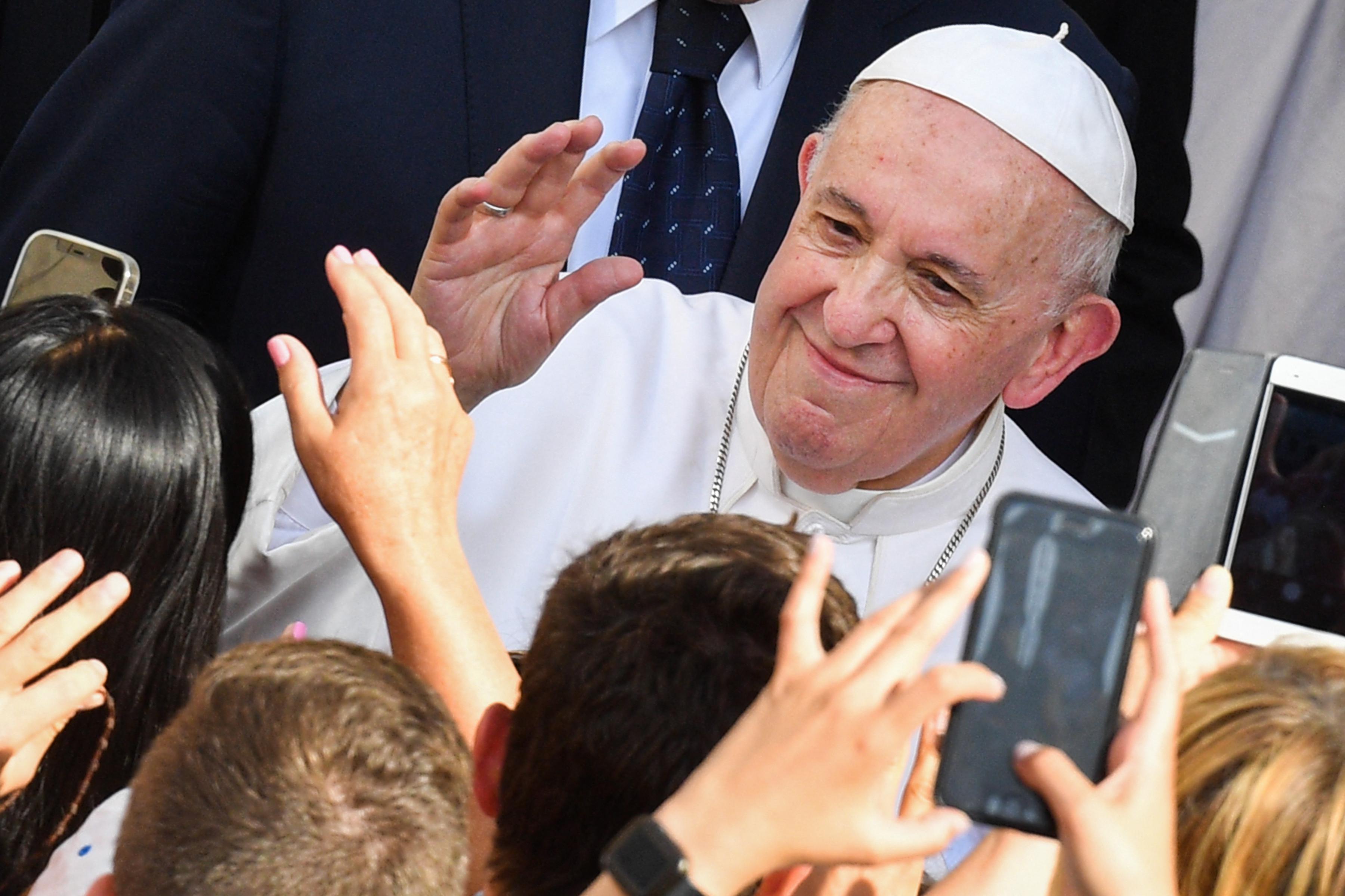 Pope Francis waves as a crowd of people reach for him and take photos.