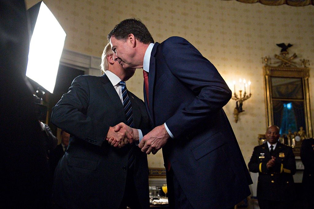 Trump and Comey shake hands as Trump speaks into Comey's ear.