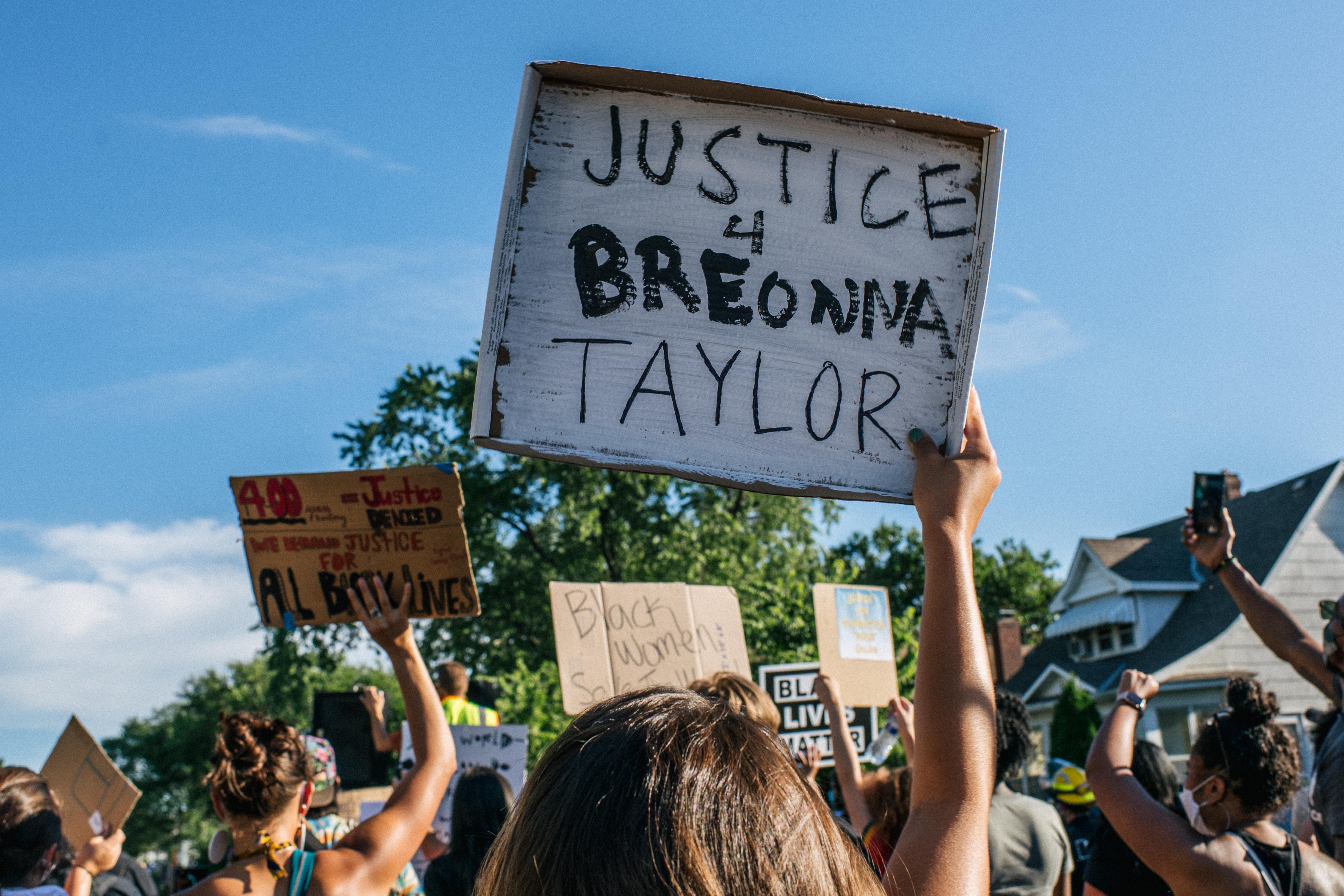 People march in a protest against police brutality and racism. One holds up a sign that reads "Justice 4 Breonna Taylor."