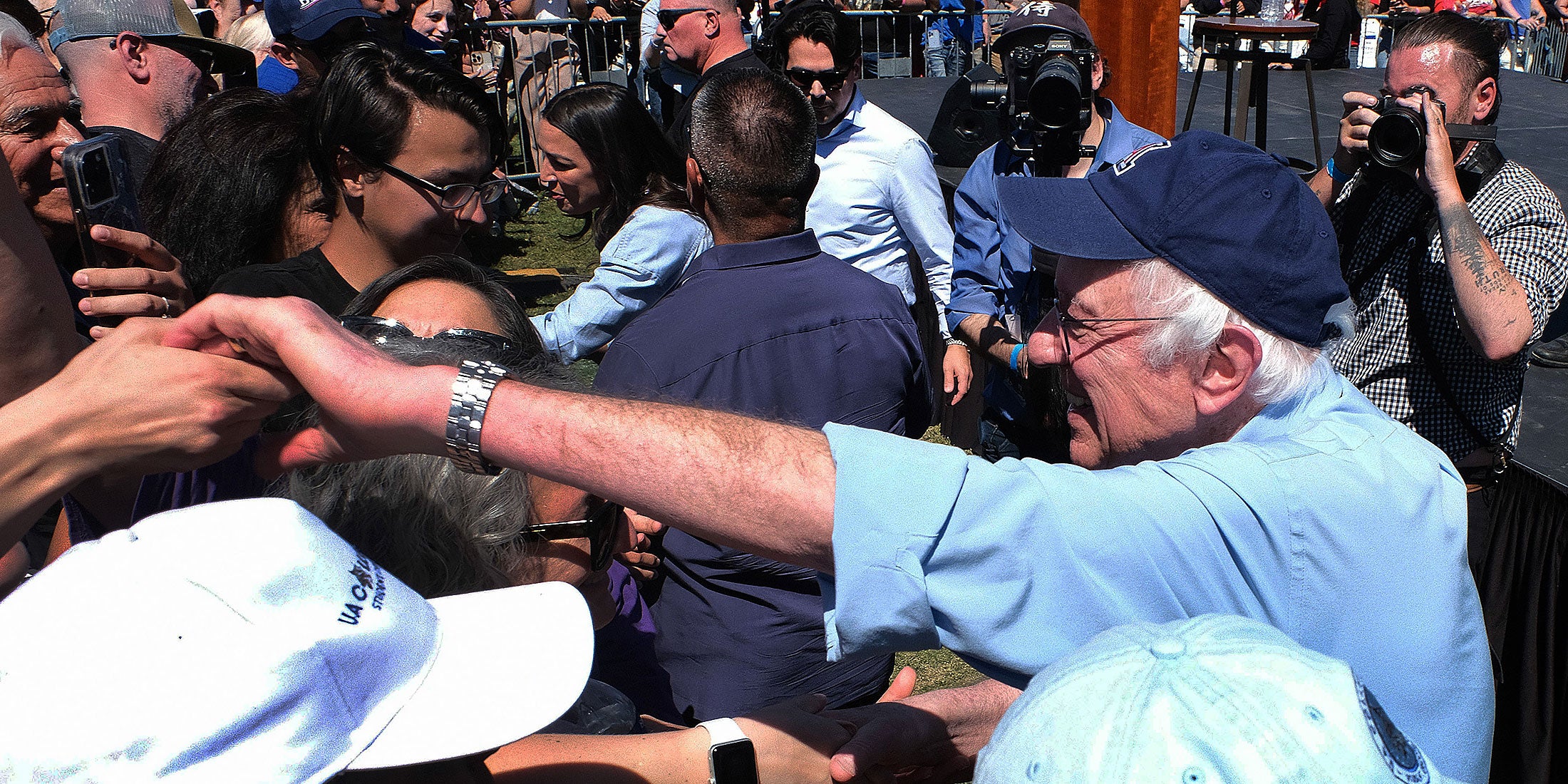 Bernie and AOC wade into an excited crowd, shaking hands.