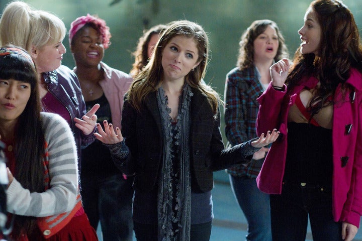 Anna Kendrick stands in a group of women shrugging her shoulders.