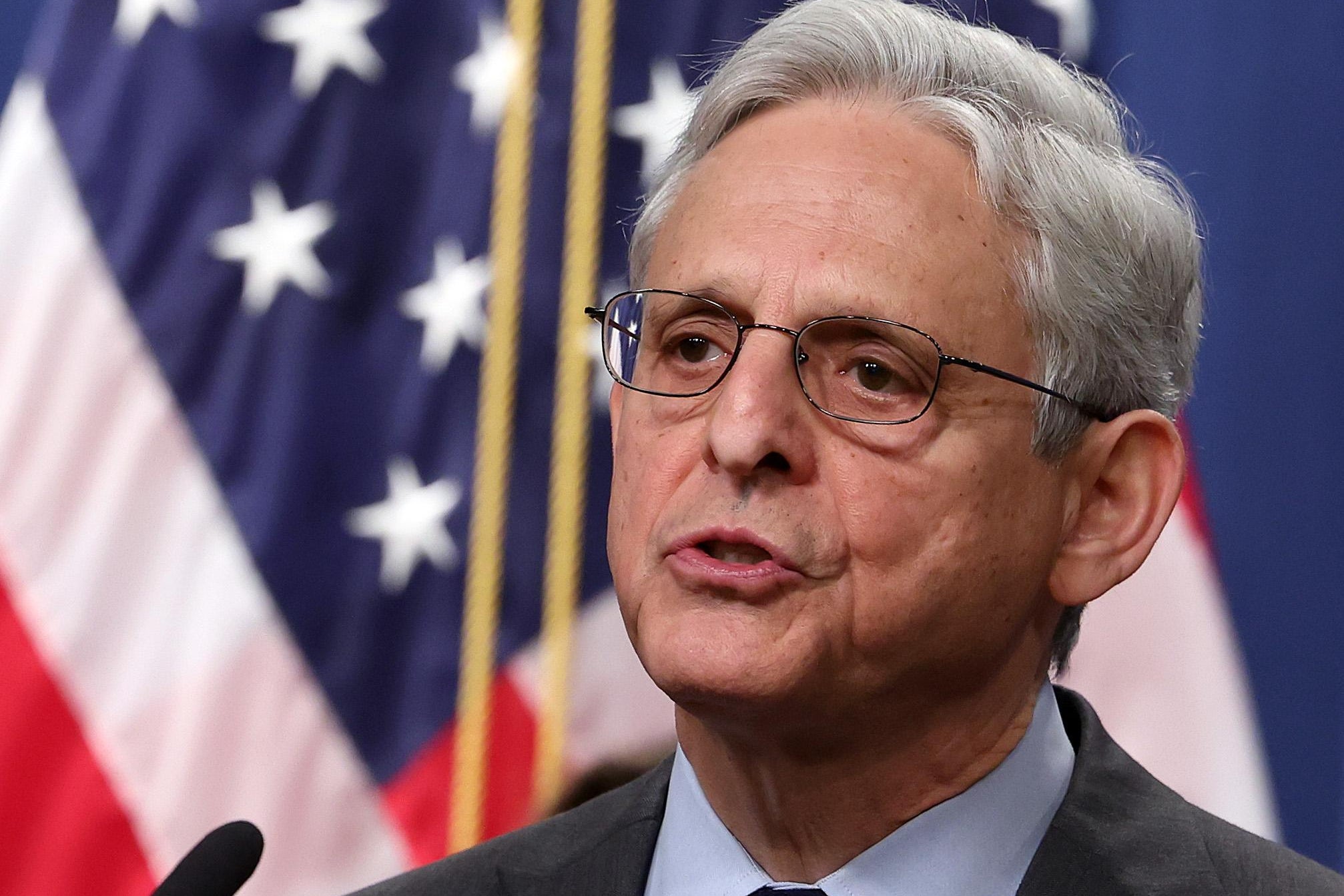 Garland with wire glasses and a suit speaks at a podium.