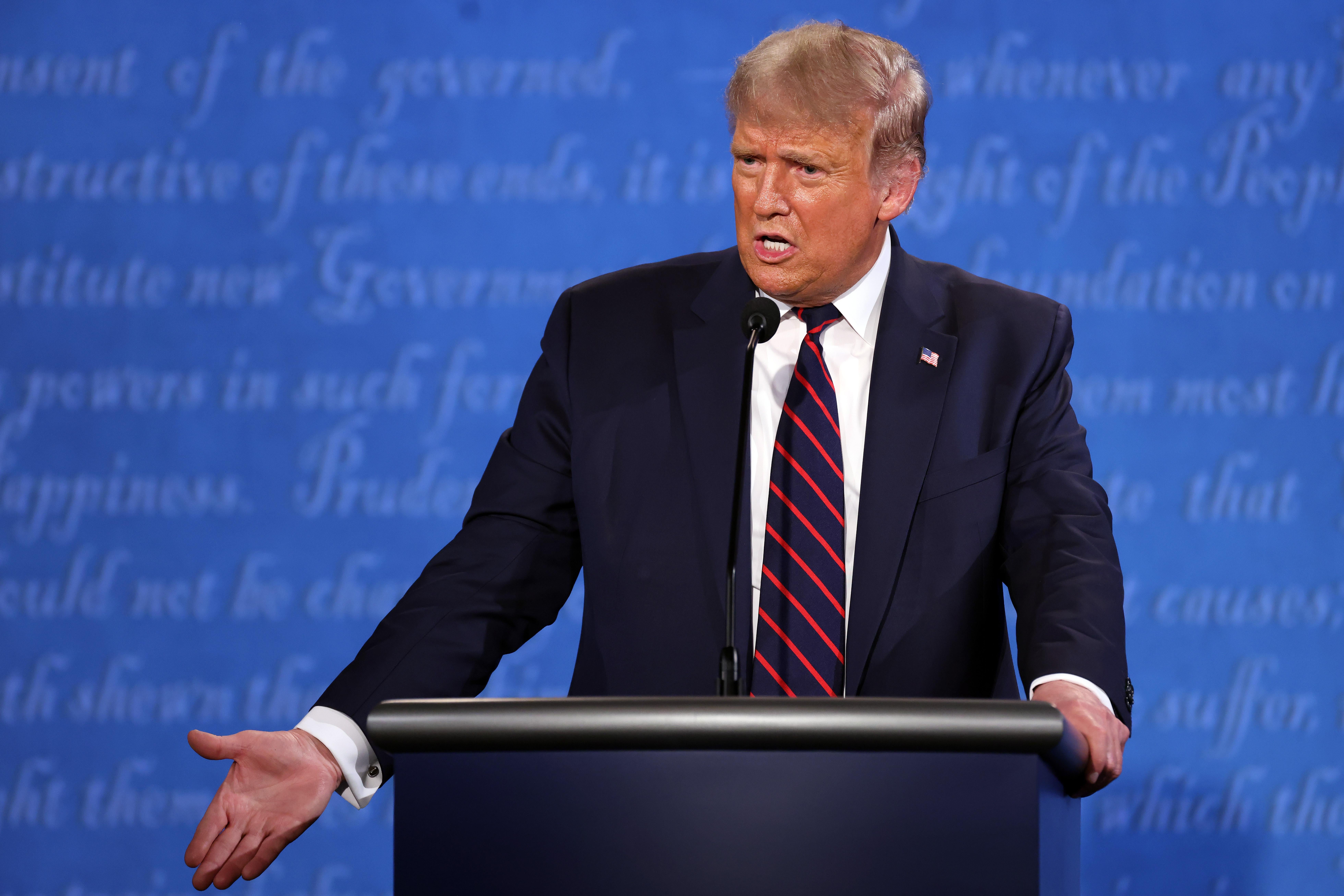 Trump gestures with his right hand as he stands at the podium on stage, answering a debate question.