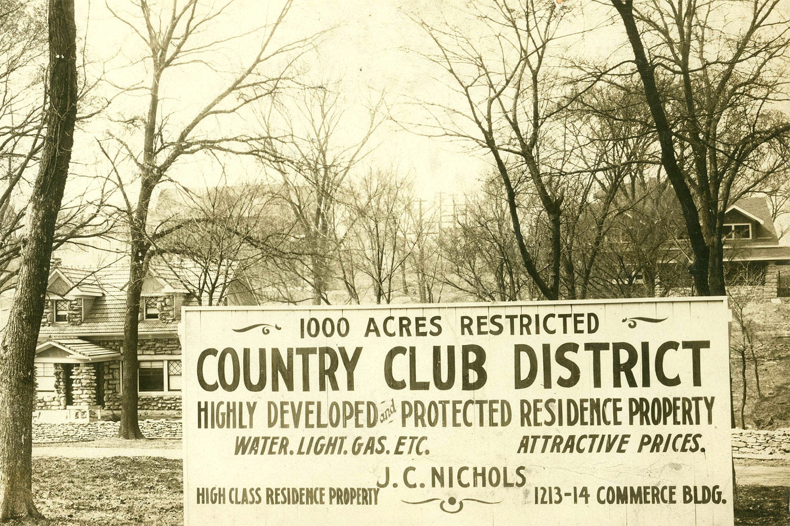 Neighborhood street with a sign that reads "1,000 Acres Restricted: Country Club District—Highly Developed and Protected Residence Property. Water, Light, Gas, Etc. Attractive Prices."