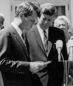 President John F. Kennedy listens as his brother Robert speak at a White House ceremony.