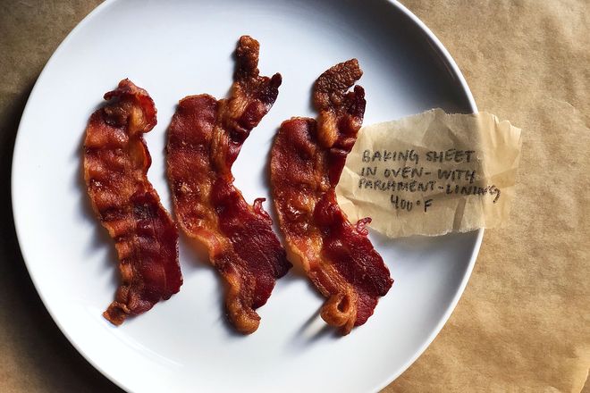 Bacon on a plate with a label: Baking Sheet in Oven - With Parchment Lining 400 degrees F. The strips are very curvy and bumpy as well as darker in color than in previous photographs.