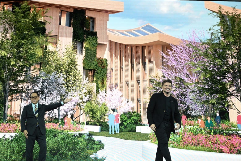 Two men stand before a large photo of a city prototype with trees and buildings.