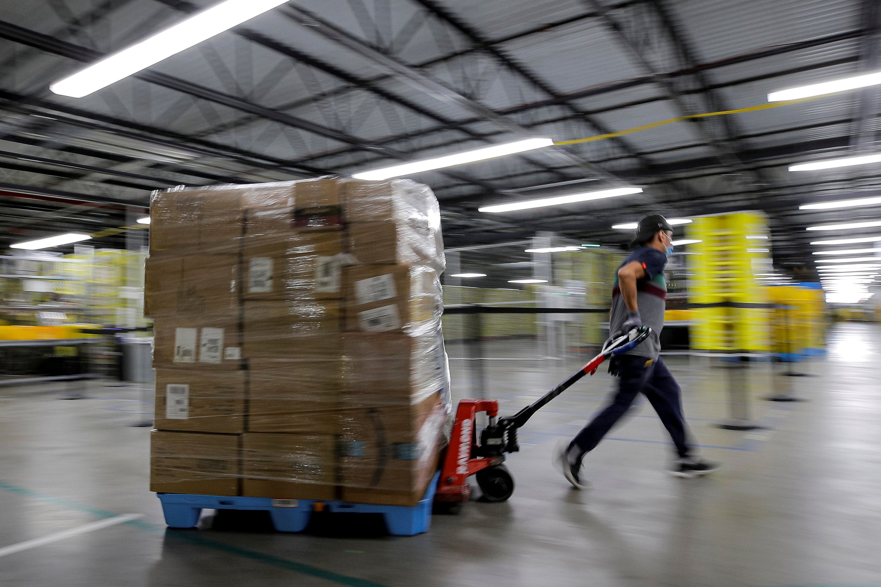 A worker pulls a cart piled high with Amazon packages through a warehouse