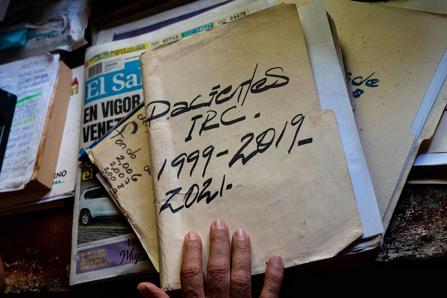 Three manila folders stacked on a table above a newspaper. The top folder reads "Pacientes 1999 - 2019, 2021 -"