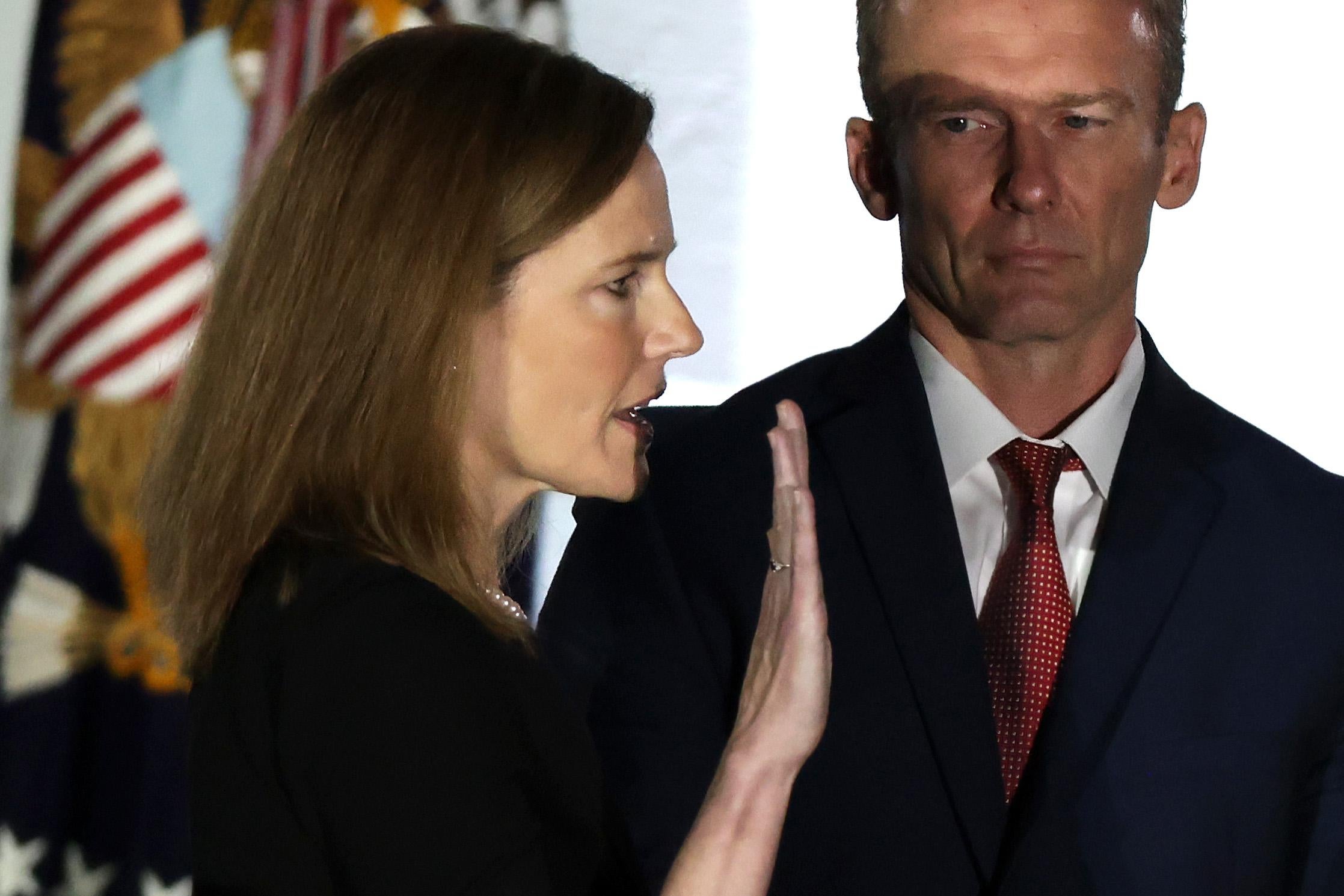 Amy Coney Barrett holds up her right hand and takes the oath as her husband looks on