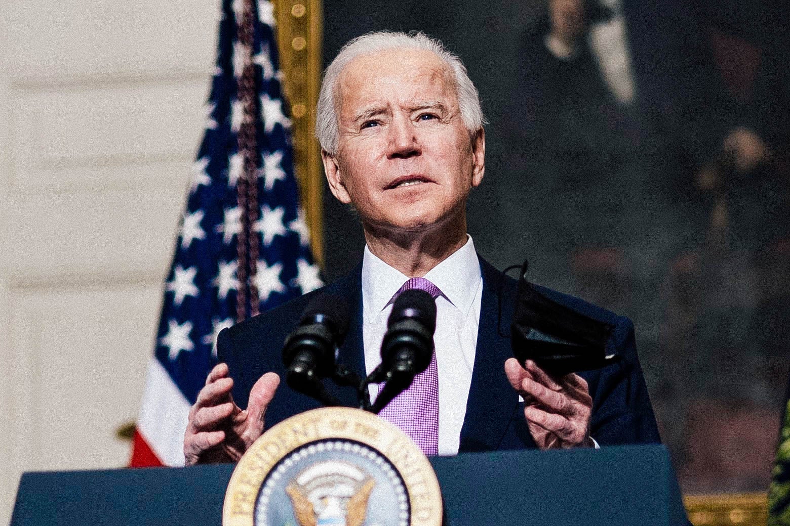 Biden gestures while speaking at a podium, with an American flag and a portrait of Abraham Lincoln in the background
