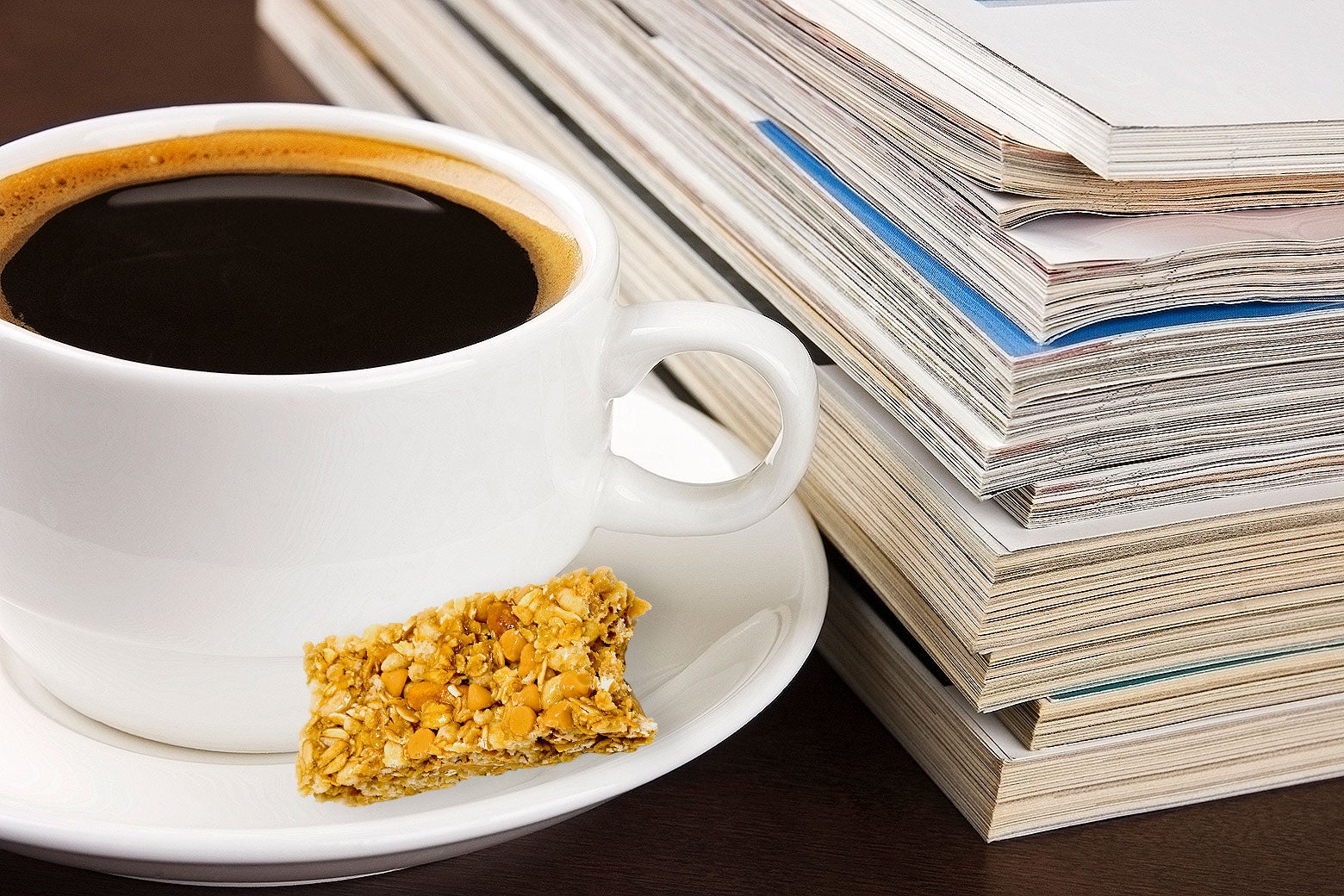A cup of coffee and part of a protein bar sitting next to a stack of work papers on a desk.