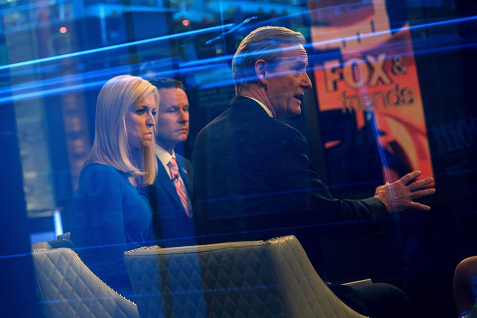 Seen through a window, (L to R) hosts Ainsley Earhardt, Brian Kilmeade and Steve Doocy broadcast Fox and Friends from the Fox News studios in New York City.