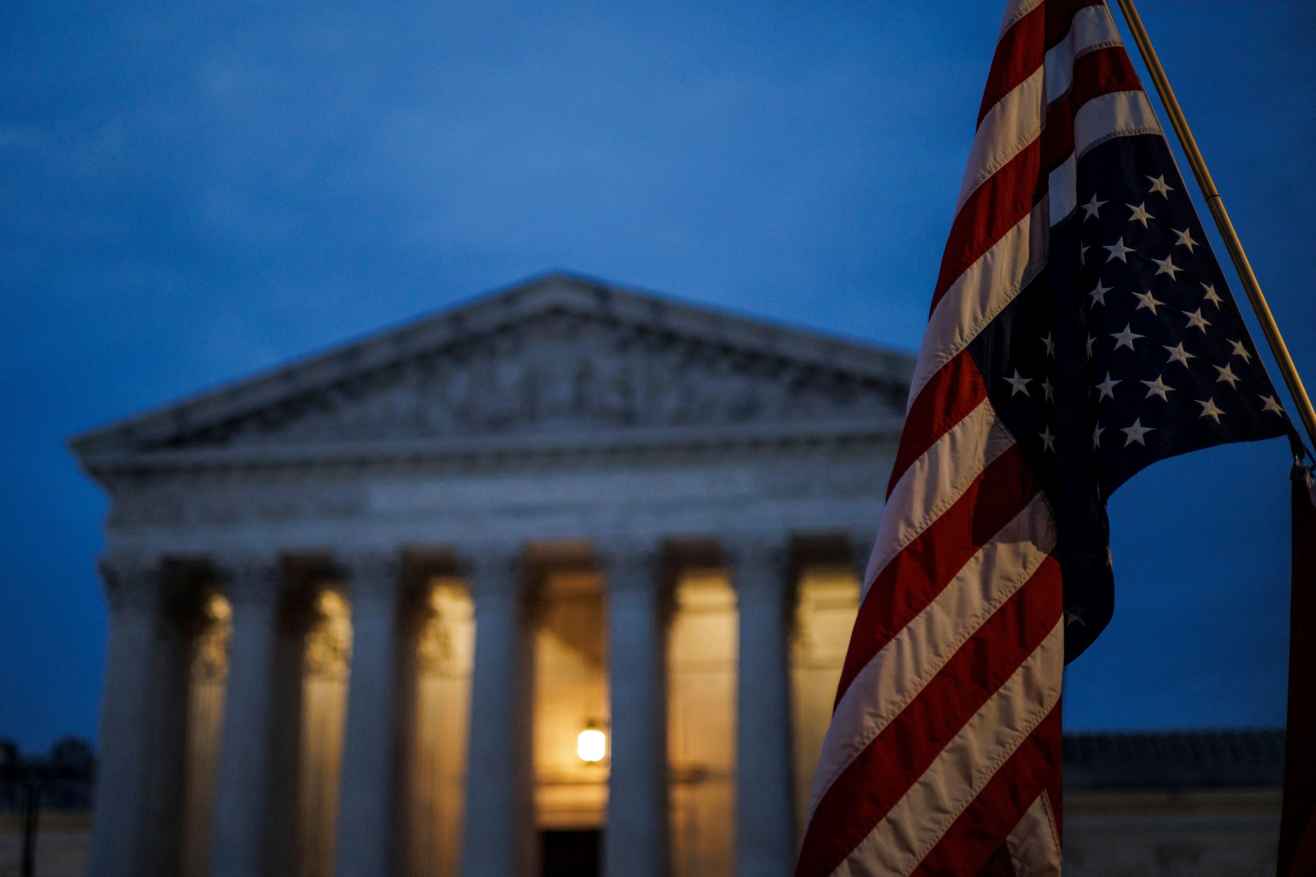 An American flag flying upside-down in front of the Supreme Court at night
