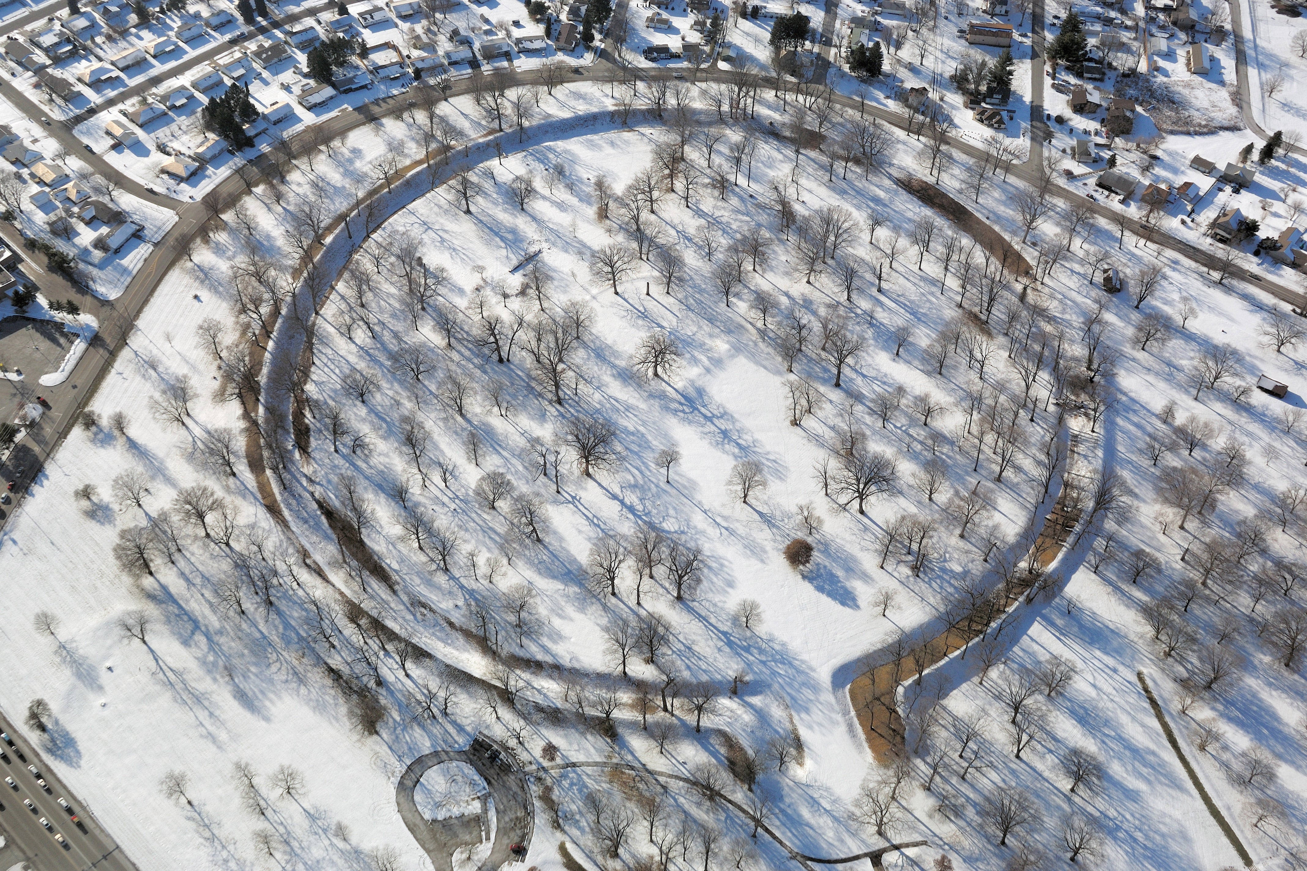 An aerial view of a snowy landscape with trees and a circular path carved through the snow. 