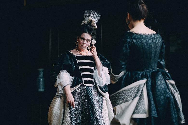 Olivia Colman, in period garb, peers into a tiny mirror.