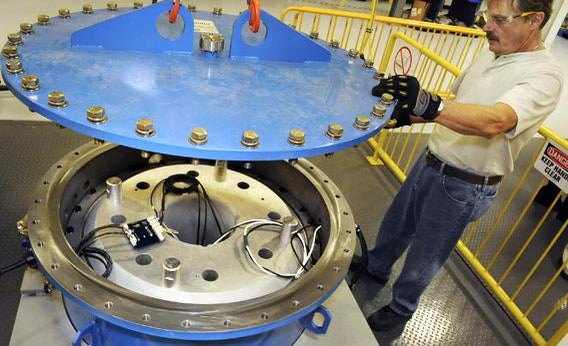 Engineering aide putting a cover on a flywheel which is a form of alternative energy.