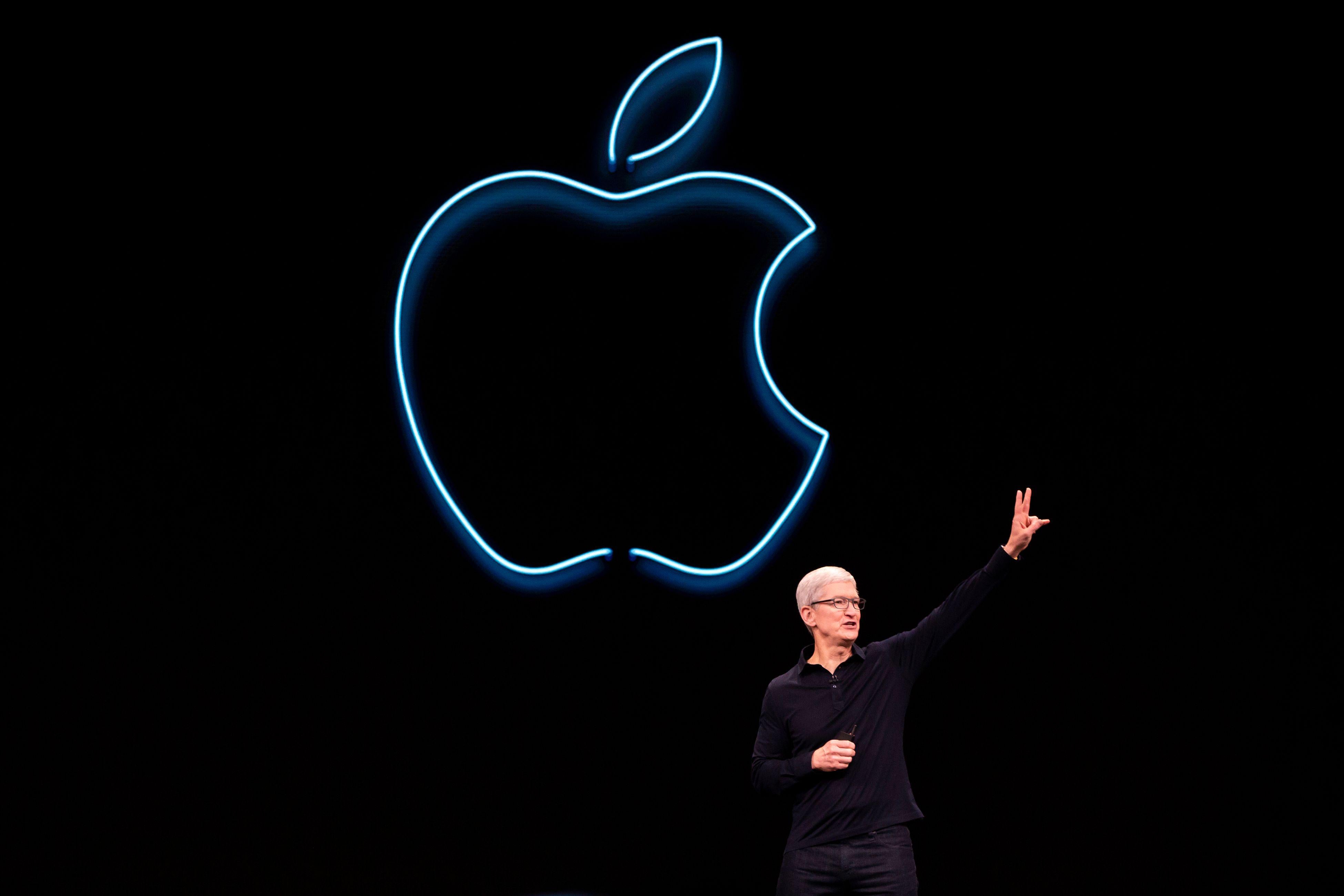 Tim Cook on a stage gesturing in front of a neon Apple logo.