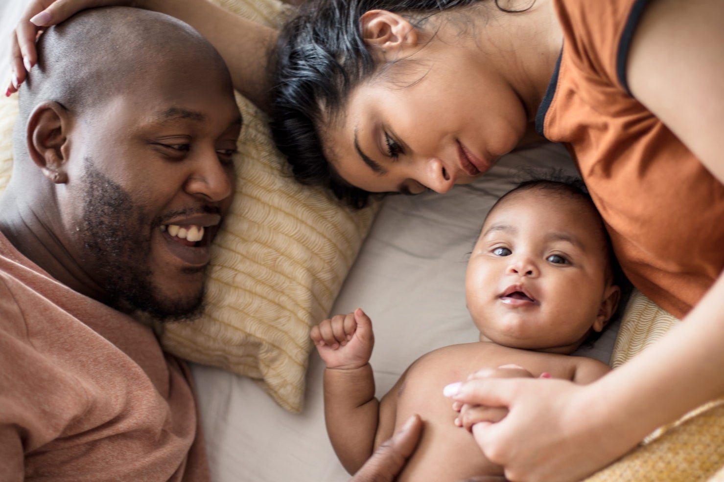 A father and mother in bed with a smiling baby