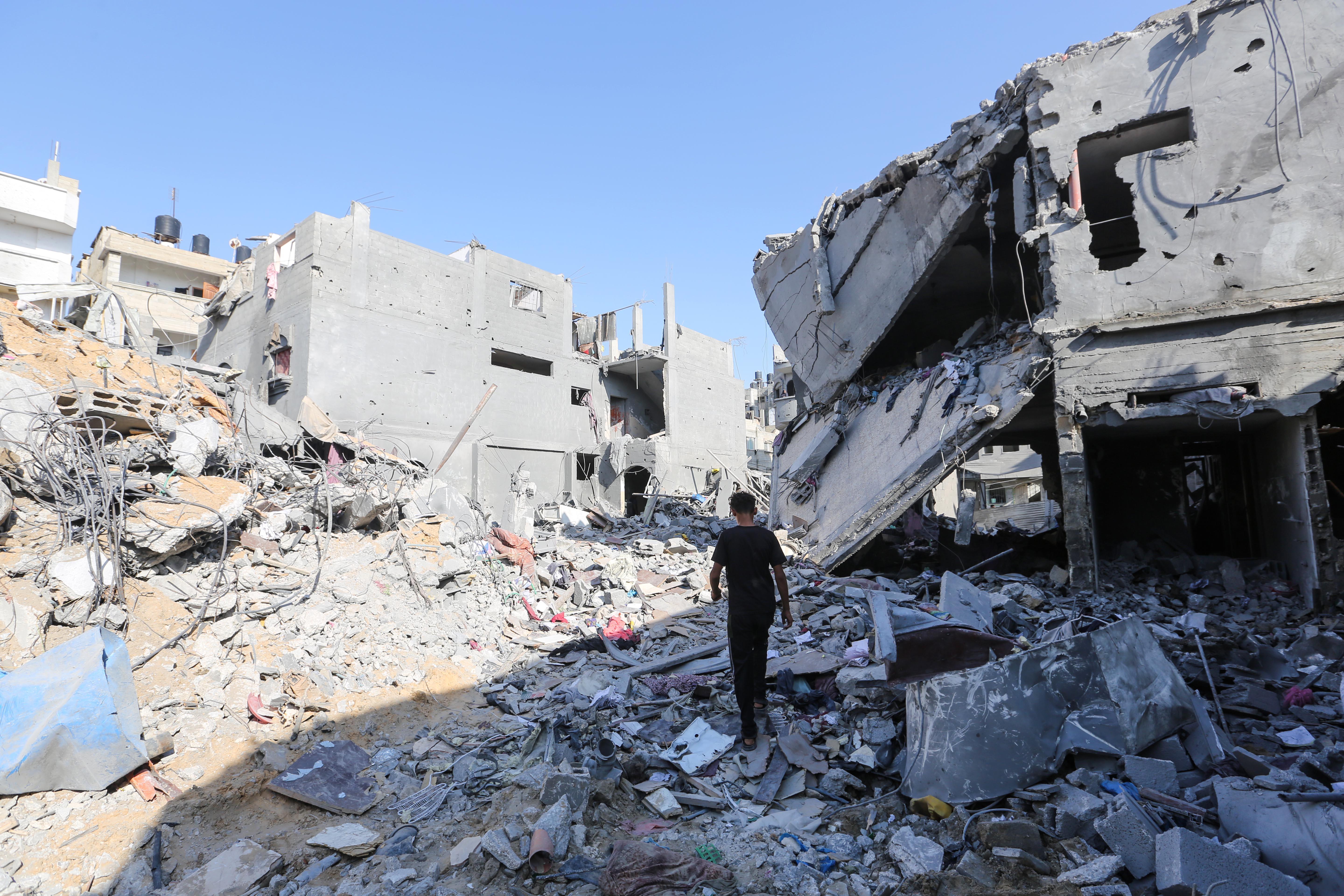 A person walks through the rubble between destroyed buildings.