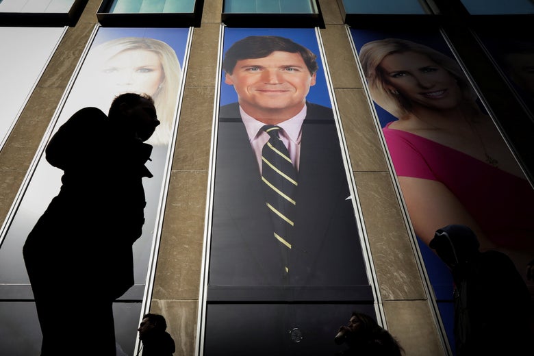 A banner of Fox News host Tucker Carlson on the side of a building, partially in shadow