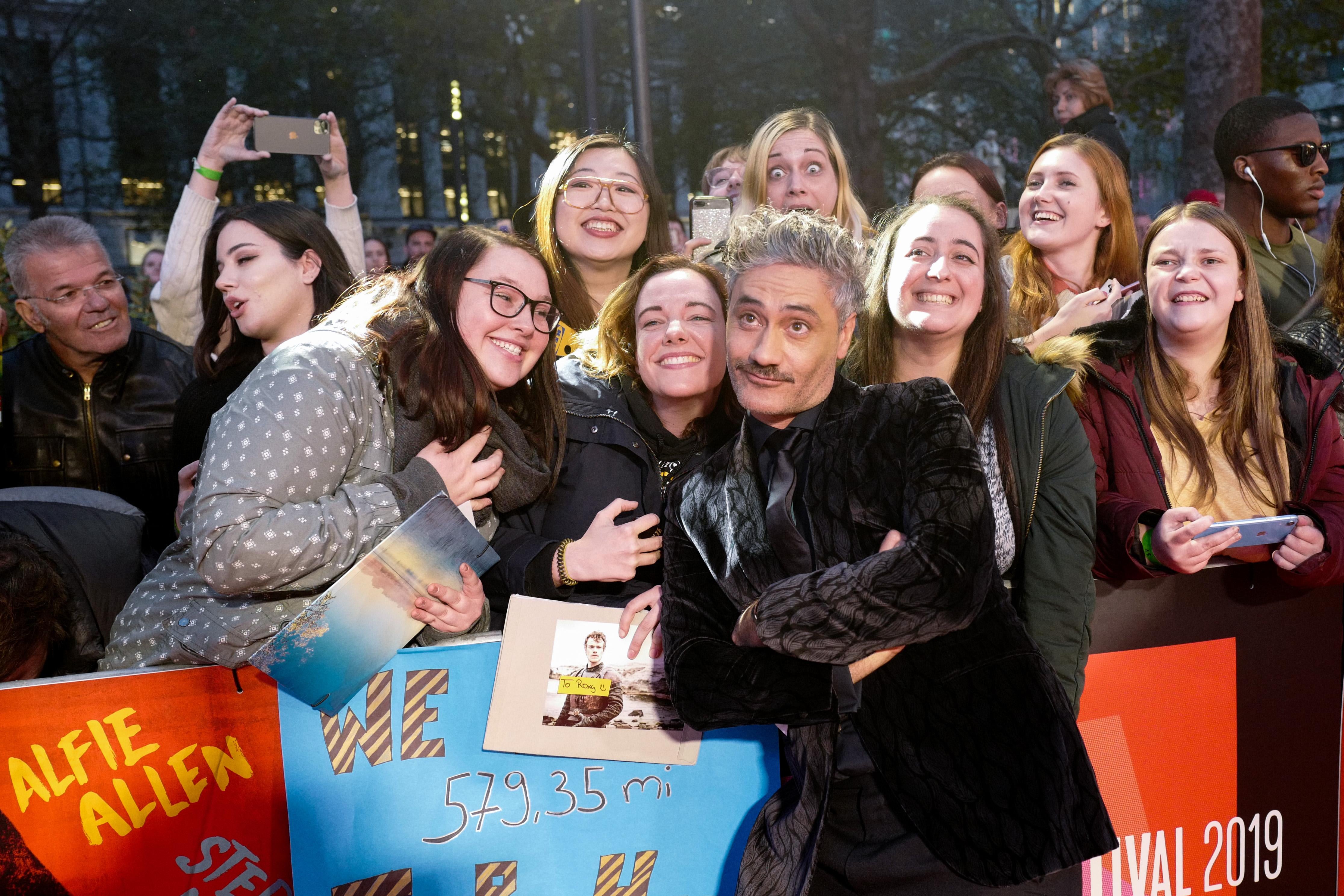 Taika Waititi mugs for the cameras on the red carpet surrounded by teens.