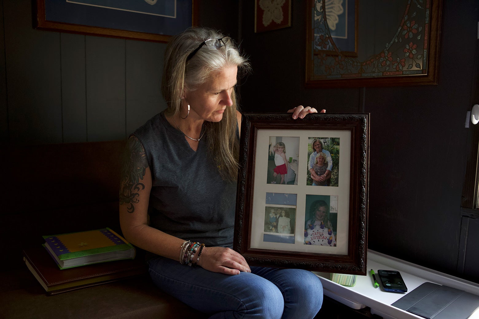 A woman with long gray hair holds up and looks at a frame of several family photos.