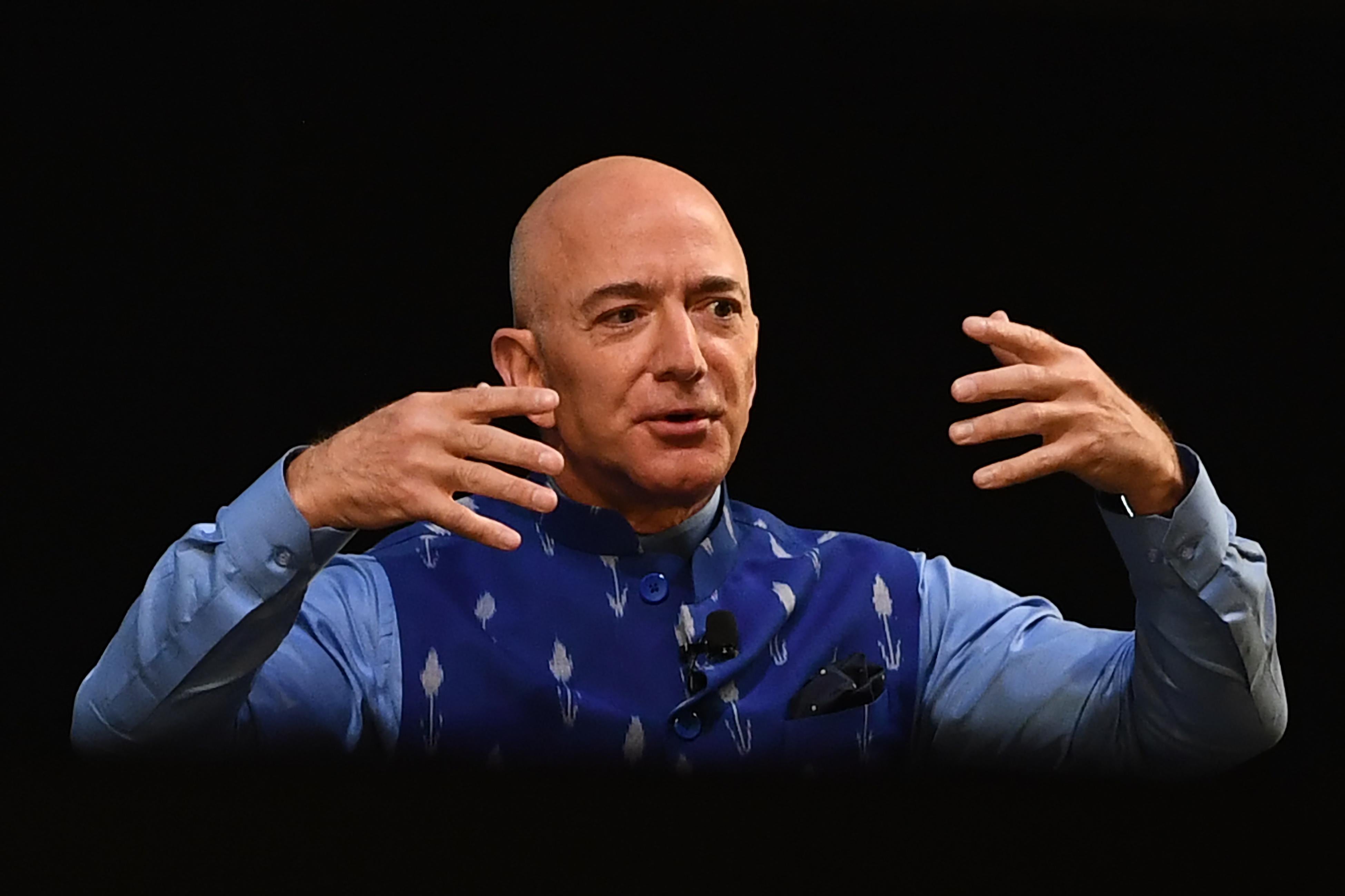 Jeff Bezos gestures with his arms raised against a black background.
