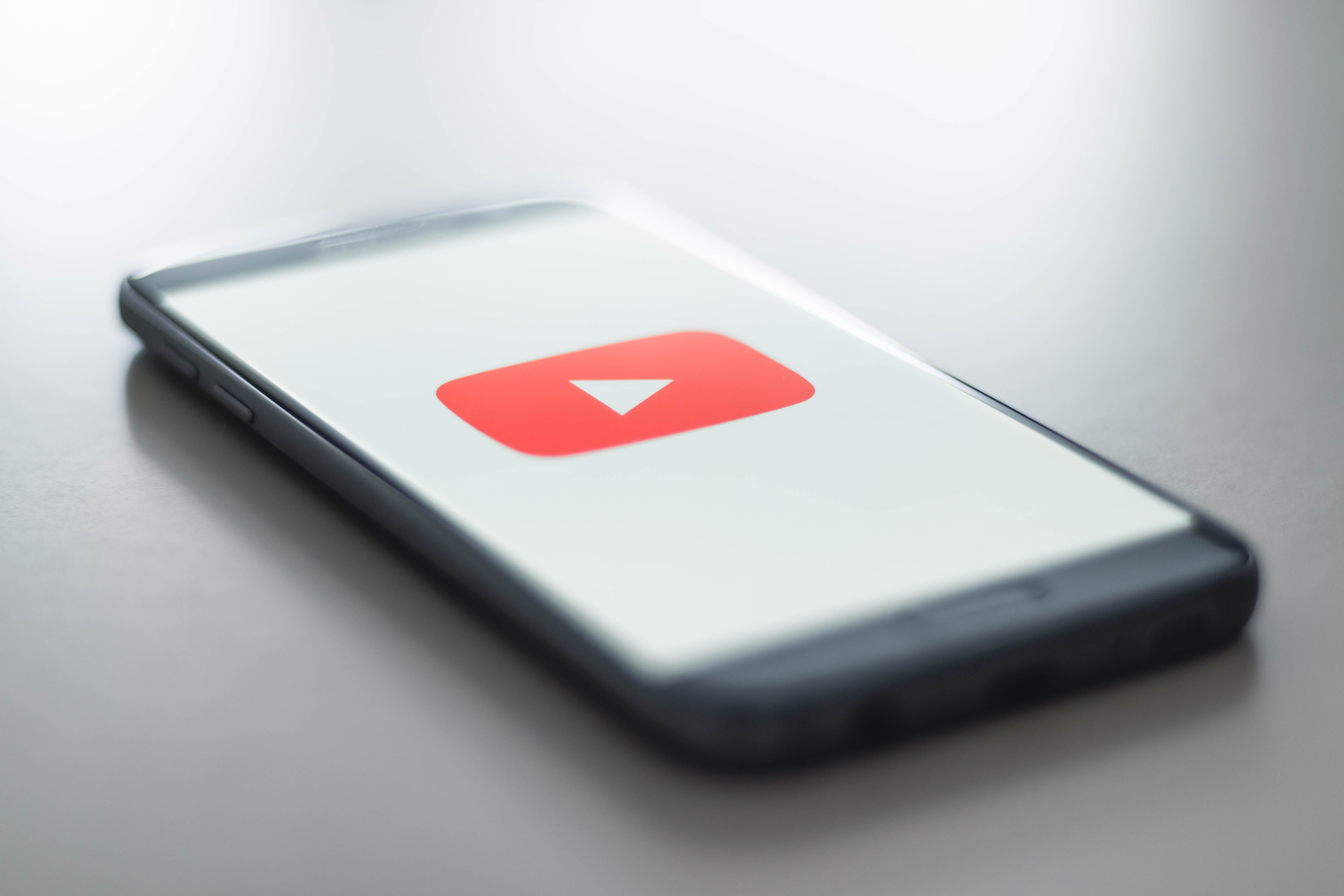 A phone sits on a flat surface. The phone is displaying the YouTube "play" video symbol of a red box with a white triangle.