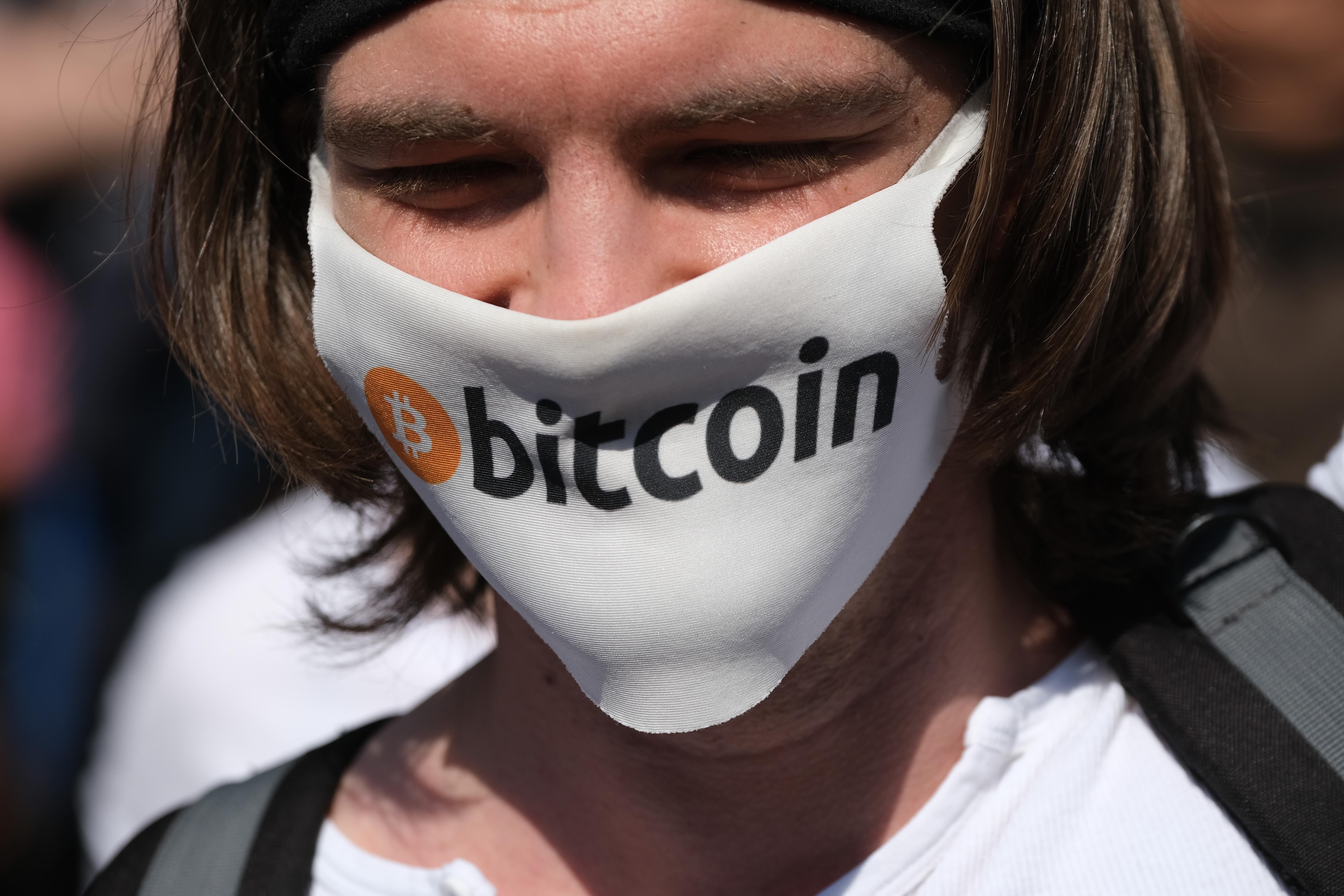  A man wears a mask with the Bitcoin logo .