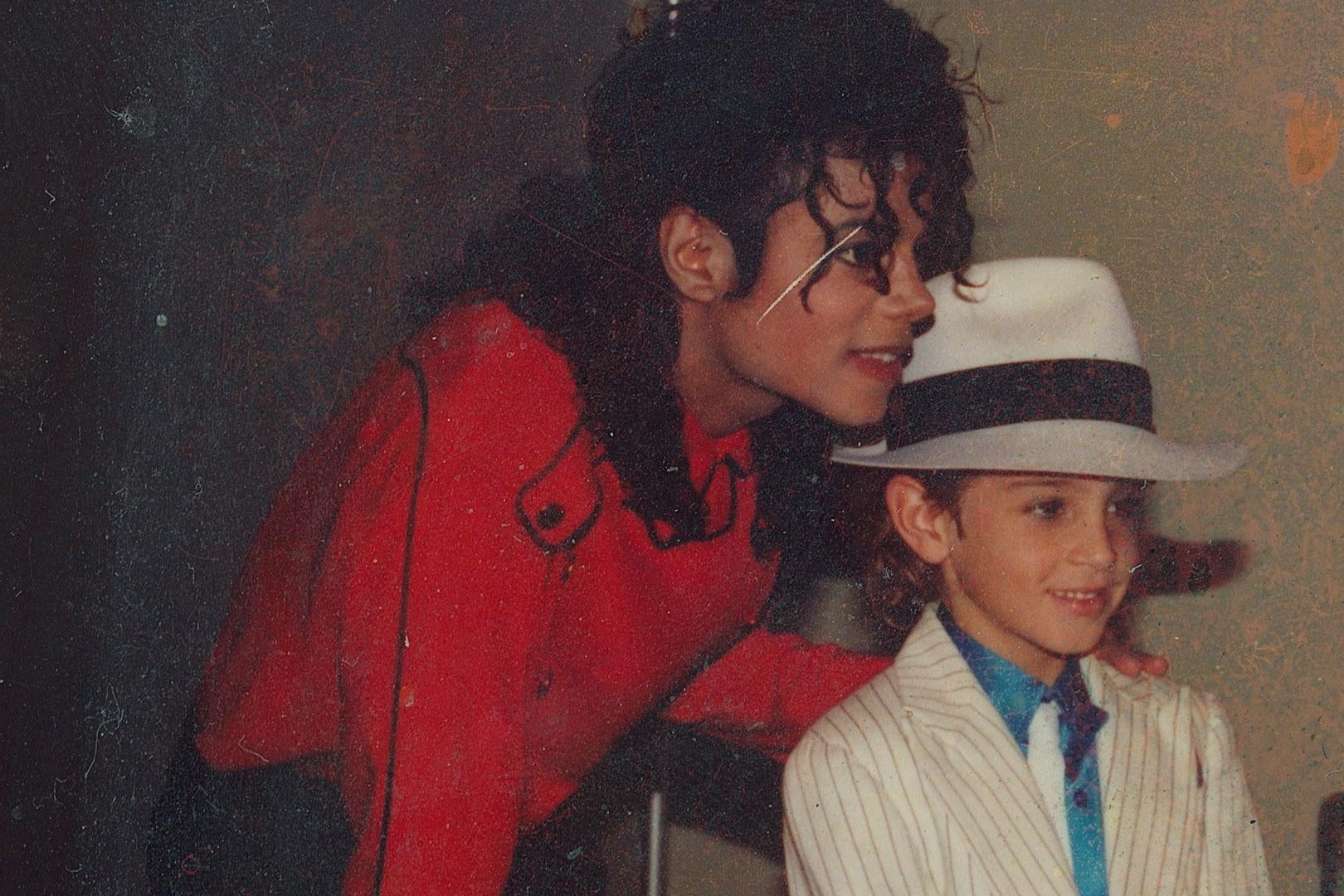 Michael Jackson in a red shirt poses with a child, Wade Robson, dressed in an outfit similar to Jackson's Smooth Criminal persona.