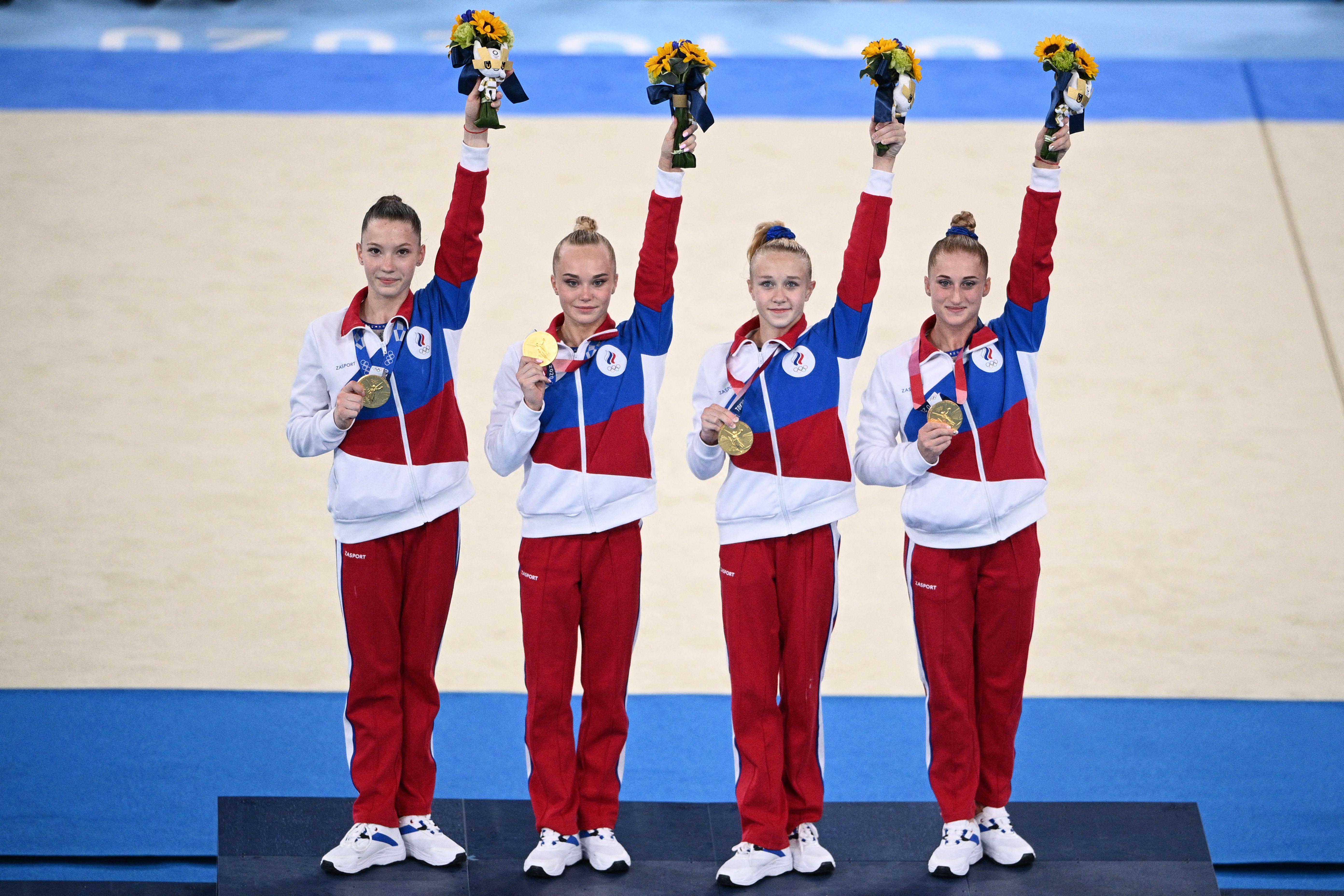 Four women on a podium raise bouquets of flowers in a victory gesture.